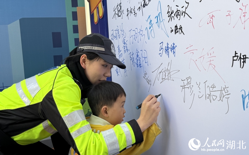 歲的小男孩在交警小姐姐帶領(lǐng)下，在文明禮讓承諾墻簽下自己的大名。人民網(wǎng)記者 周恬攝